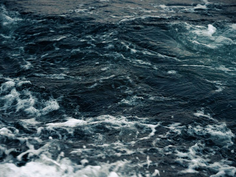A dark sea under a low horizon, the water moving in long quiet bands.