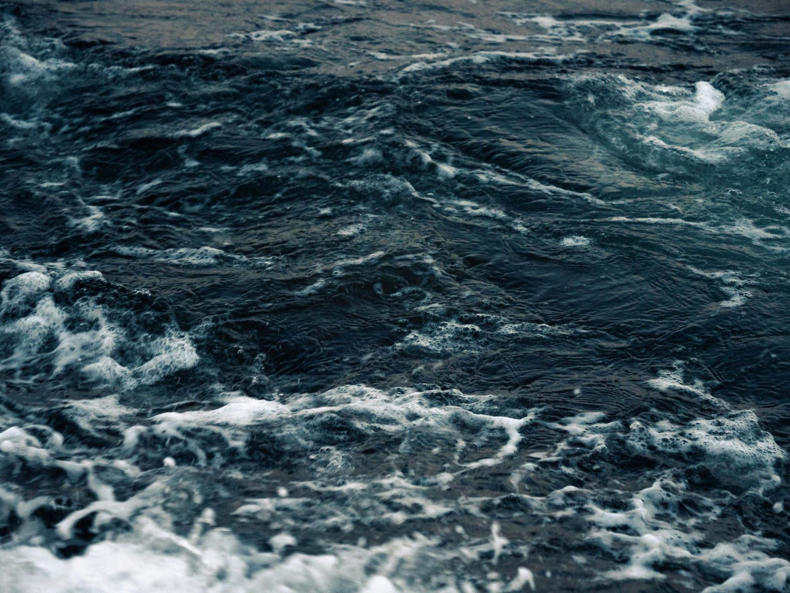 A dark sea under a low horizon, the water moving in long quiet bands.