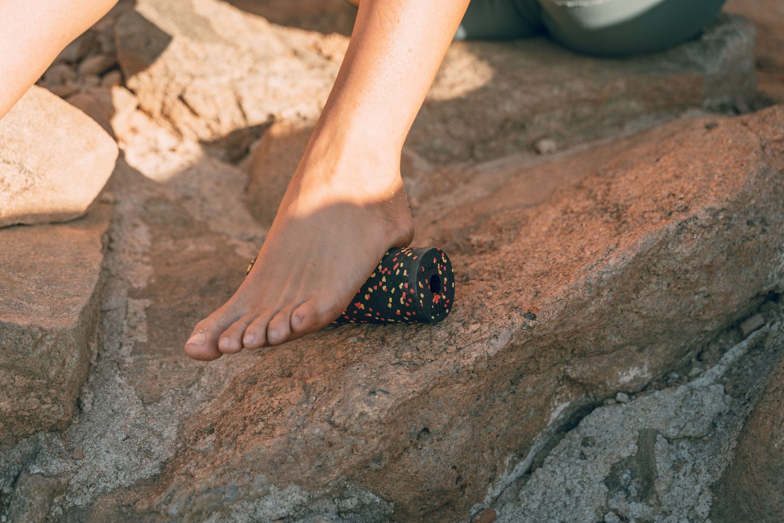 A bare foot resting on a small soft therapy ball on a wooden floor.