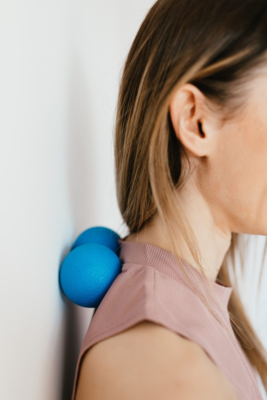 A small therapy ball resting against the back of the neck, hands supporting, in soft light.