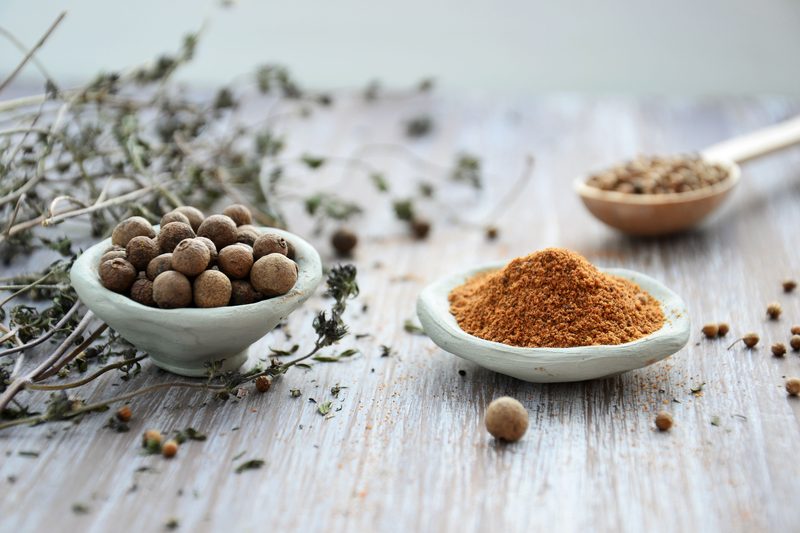 Small handmade clay bowls of allspice and ground spice on a weathered wooden table, with sprigs of dried thyme.